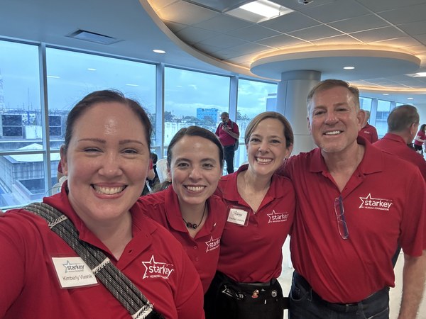 Group of four people, with red shirts on smiling at the camera while volunteering 